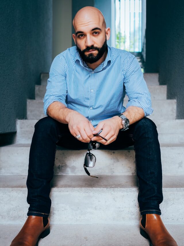 man in blue and white checkered dress shirt and black denim jeans sitting on concrete bench