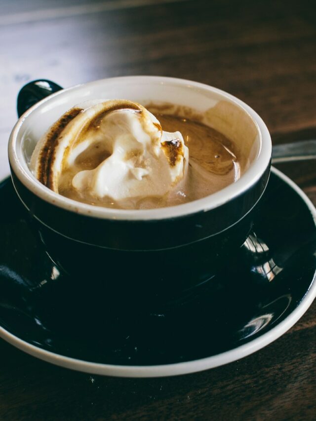 white and black ceramic mug filled with brown latte on round black ceramic saucer