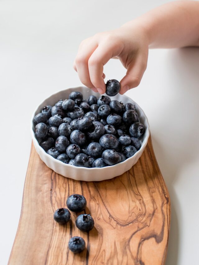 person holding bowl of black berries