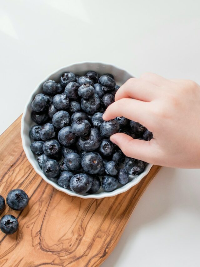 person holding blue berries in white ceramic bowl