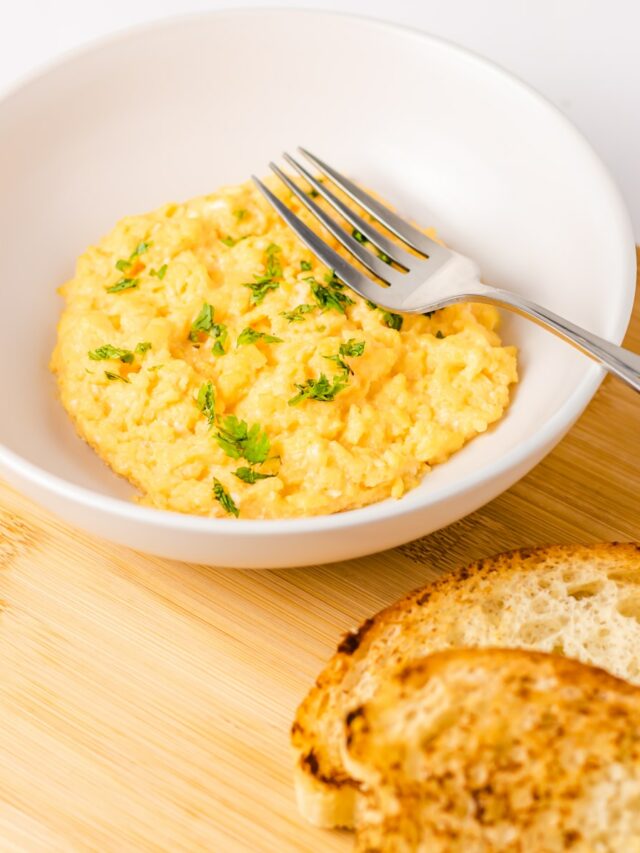 a bowl of scrambled eggs next to a slice of bread