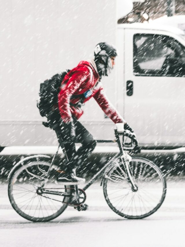 person in red jacket riding on mountain bike with white vehicle nearby during winter