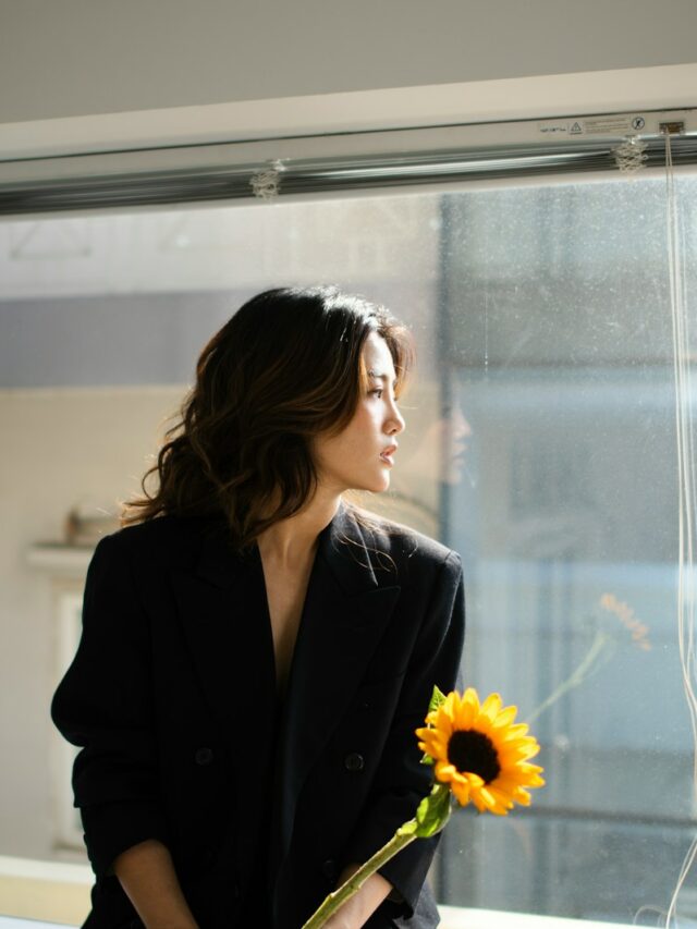 A woman standing in front of a window with a sunflower in her hand